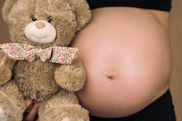 A pregnant girl holds a Teddy bear in her hands