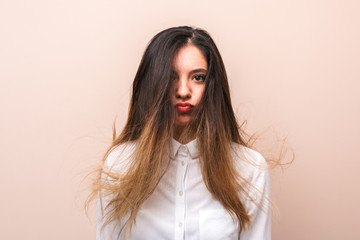 attractive brunette in white shirt with flying hairs makes funny face against pink background. studio shoot