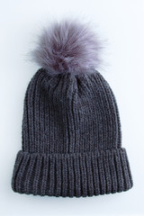 Fototapeta na wymiar Woolen dark gray hat with fur pompom on a white background.