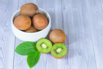 fresh kiwis in a white bowl on the table close-up. background with whole kiwis, kiwi halves and green leaves. background with tropical fruits.