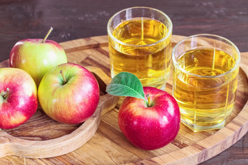 glasses of apple juice and fresh apples on a wooden tray close-up. background with ripe red apples and apple juice in glasses.