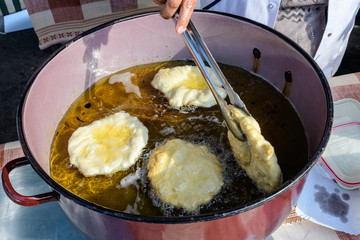 Donuts being deep fried in boiling oil in a large pan, at a street food market, selective focus