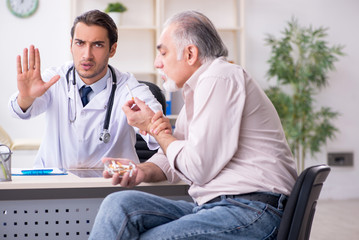 Young male doctor and old patient in antismoking concept