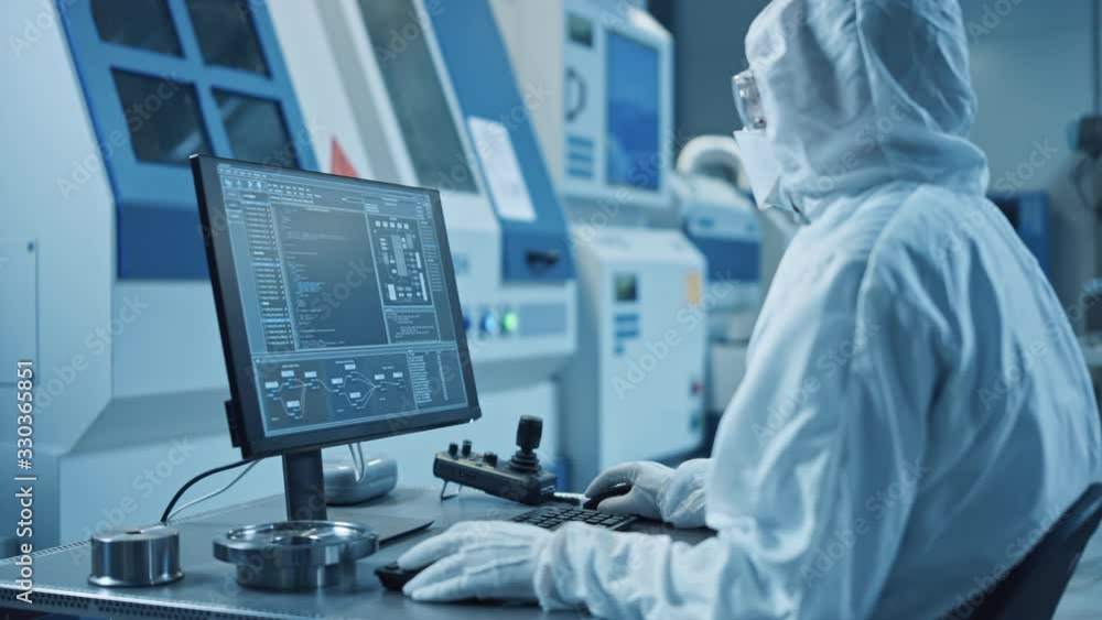 Poster factory cleanroom: engineer wearing coverall and does system control on pc, uses controller, screen 