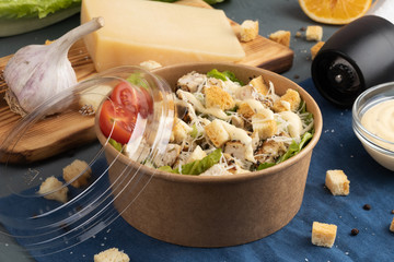Caesar salad in eco packaging with an open lid on blue textile in the interior