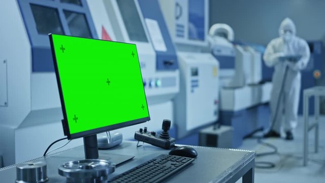 Factory Cleanroom: On the Desk Personal Computer Showing Green Screen Chroma Key Display. In Background CNC Machinery, Professionals Use Robot Arm on Production Line. Zoom in Shot