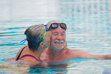 couple of two seniors doing exercise together to be and have a healthy and fit lifestyle - pensioners and mature people swimming in the pool and woman kissing the man