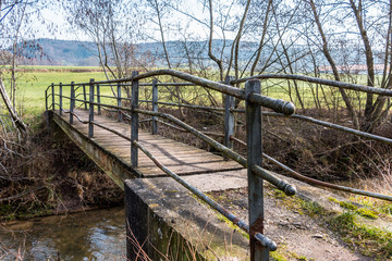 Fototapeta na wymiar Little iron bridge across the little river and a green meadow