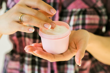 Female hands holding natural white smooth cream, touching it with finger. Cosmetic product and beauty skincare concept. Blank pink container.