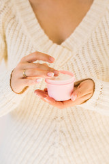 Close up of woman holding natural white smooth cream. Cosmetic product and beauty skincare concept. Blank pink container. Cream and female hands.