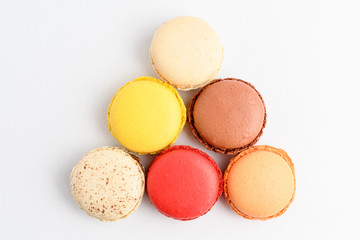 Top view of row of six sweet French macarons with different aromas, isolated on white, flavours of lemon, caramel, vanilla, orange and chocolate, tasty dessert in pastel colors on a table
