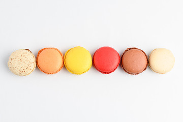 Row of six sweet French macarons with different aromas, isolated on white, flavours of strawberries, lemon, caramel, vanilla, orange and chocolate, tasty dessert in pastel colors on a table