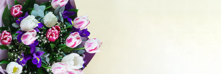 A bright spring bouquet with tulips and irises in a gift box lies on the yellow table