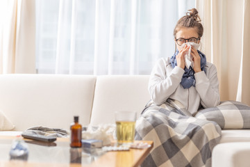 Ill teen with runny nose sitting on a sofa at home and sniffling because of cold and fever. she has...