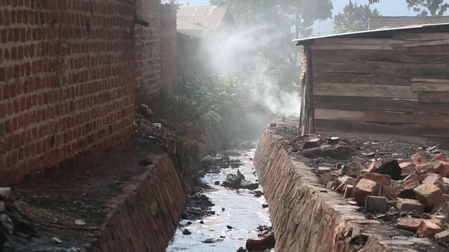 Sewage Ditch in African Town as Smoke Comes Out of Home Nearby