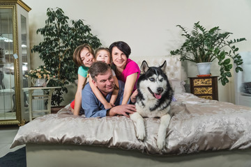 Happy family together with a dog lie on a large bed indoors.