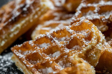 Homemade sweet waffles in the shape of a heart, with powdered sugar. Close up on black surface.