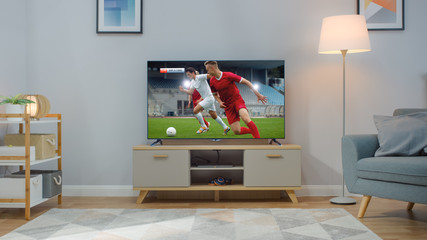 Shot of a TV with Soccer Match. Cozy Bright Living Room with a Chair and Lamps Turned On at Home.