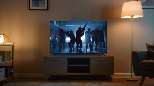 Shot of a TV with an Action Movie with Soldiers. It's Evening and Room at Home Has Working Lamps.