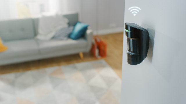 Close Up Object Shot of a Modern Movement Detector Unit with Digital Icon of Wireless Connection on a White Wall in a Cozy Apartment in the Background.