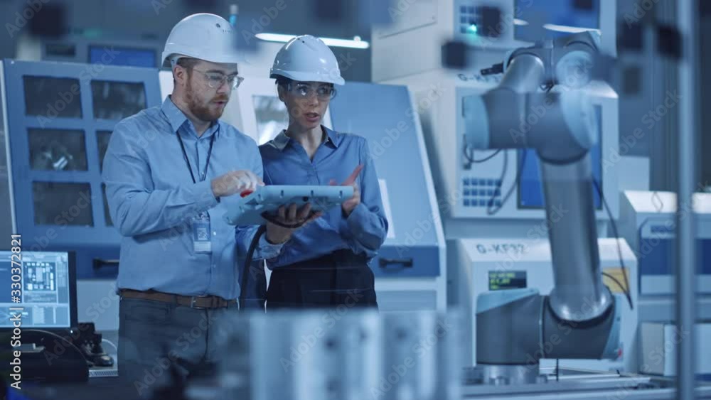 Poster Factory Workshop: Professional Female Engineer, Male Machinery Operator Use Industrial Digital Tablet Computer to Work and Program Robot Arm for Production Line. High-Tech Facility with CNC Machines