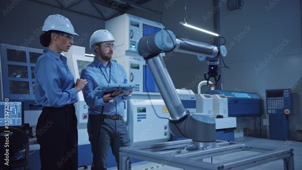 Poster Factory Workshop: Professional Female Engineer, Male Machinery Operator Use Industrial Digital Tablet Computer to Work and Program Robot Arm for Production Line. High-Tech Facility with CNC Machines