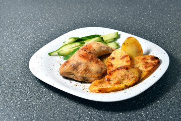 Fried chicken with potatoes on a white plate on a gray granite table