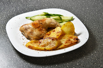 Fried chicken with potatoes on a white plate on a gray granite table