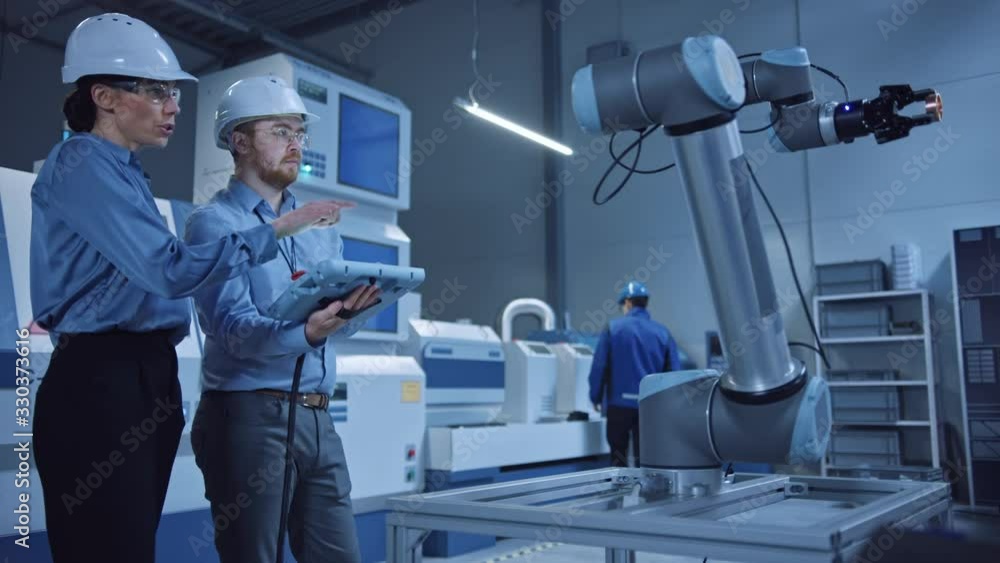 Poster Factory Workshop: Professional Female Engineer, Male Machinery Operator Use Industrial Digital Tablet Computer to Work and Program Robot Arm for Production Line. High-Tech Facility with CNC Machines