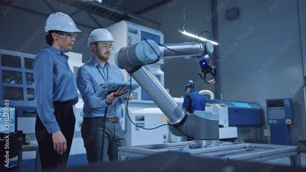 Poster Factory Workshop: Professional Female Engineer, Male Machinery Operator Use Industrial Digital Tablet Computer to Work and Program Robot Arm for Production Line. High-Tech Facility with CNC Machines