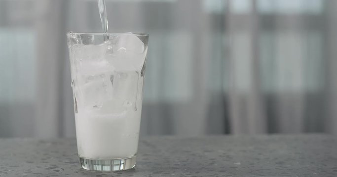 Slow motion pour soda in glass with ice cubes on concrete countertop