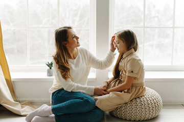 A nice cute girl and her beautiful mother enjoy sunny day. Family playing together with a rabbit in a bright sunny room