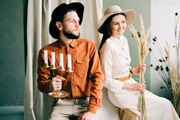 stylish couple in love with hats sitting on a brown sofa, hugging in a spacious beautiful Studio