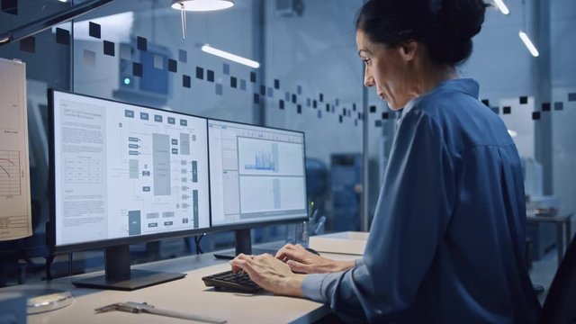 Factory Office: Portrait of Beautiful and Confident Female Industrial Engineer Working on Computer, on Screen Industrial Electronics Design Software. High Tech Facility with CNC Machinery