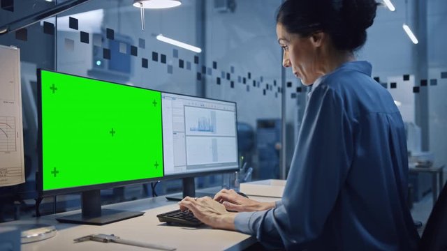 Factory Office: Portrait of Beautiful and Confident Female Industrial Engineer Working on Computer, Green Screen Chroma Key Display. High Tech Facility with CNC Machinery