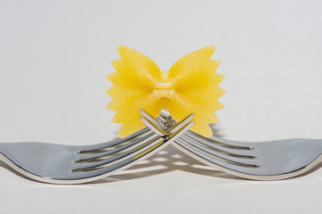 Farfalle pasta (butterflies) and silver forks on a white background.