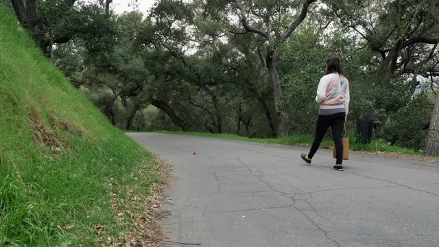 Female walking alone on a path in a park with tree all around, slow motion