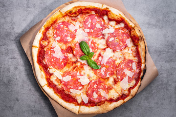 Pizza on wooden board on grey stone background. Italian traditional food. Delicious pizza with parmigiano-reggiano cheese, chorizo and basil. Restaurant menu. Copy space, top view