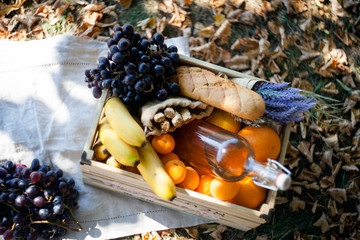 autumn picnic wooden box with fruits-grapes, bananas, Oranges and bottle of drinking water