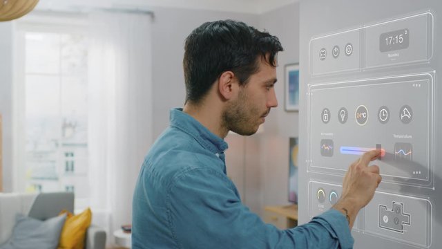 Handsome Young Man Interacts with an Augmented Reality Software. He is Setting Climate Control Unit to a Higher Temperature. Smart Home Concept with Transparent Screen Made with VFX Special Effects.