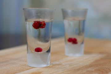 ice-cold vodka glasses with raspberries and currants on a wooden stand