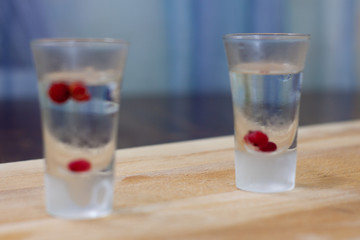 ice-cold vodka glasses with raspberries and currants on a wooden stand
