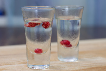 Fototapeta na wymiar ice-cold vodka glasses with raspberries and currants on a wooden stand