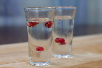ice-cold vodka glasses with raspberries and currants on a wooden stand