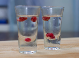 ice-cold vodka glasses with raspberries and currants on a wooden stand