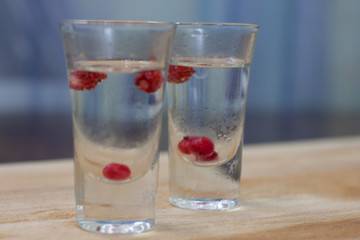 ice-cold vodka glasses with raspberries and currants on a wooden stand