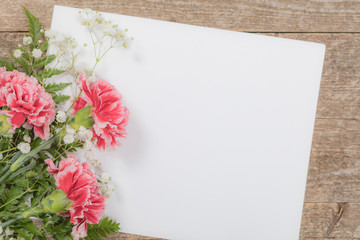 Top view of Carnation Flowers on White Vintage Wooden Background with Sheet of Paper. Design concept for Mother day, wedding and Valentine's day with copy space. Toned image. Selective focus.