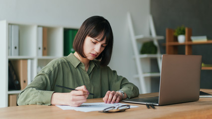 Frustrated brunette female freelancer working with laptop and making notes