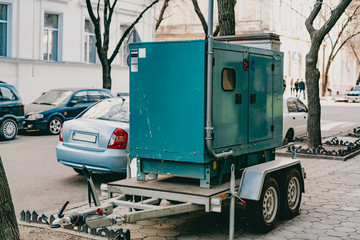 Mobile moveable gensets portable diesel engine power electric generator on a trailer stands on the city's street. Green. Urban. Electricity. Power supplier for business. Outdoor. Sidewalk. Road. Wheel