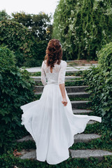 Running bride in a wedding dress for the ceremony. The view from the back. Beautiful bride from the back on a background of green nature. The bride holding dress with her hands and walking the stairs